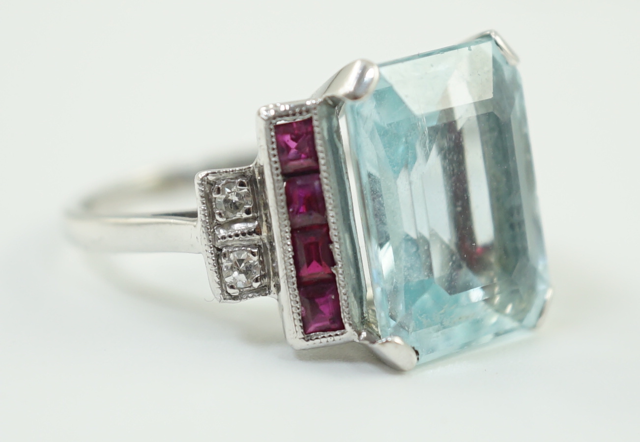 A platinum and single stone emerald cut aquamarine set dress ring, with ruby and diamond set stepped shoulders